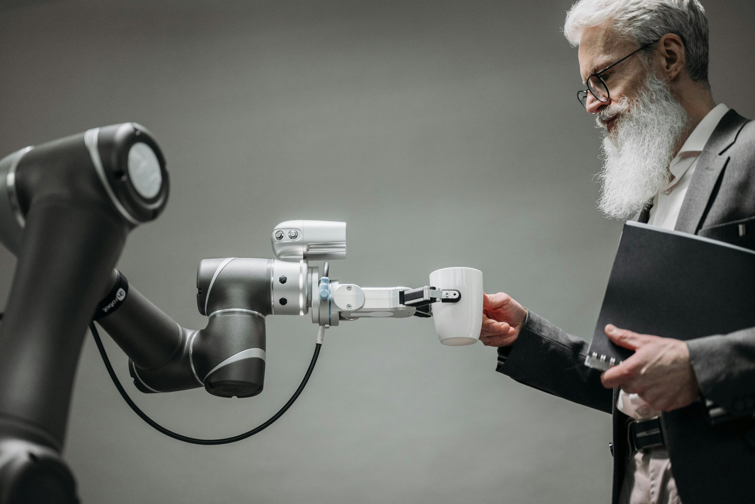 An elderly man receives a cup from a robotic arm in a modern office setting.